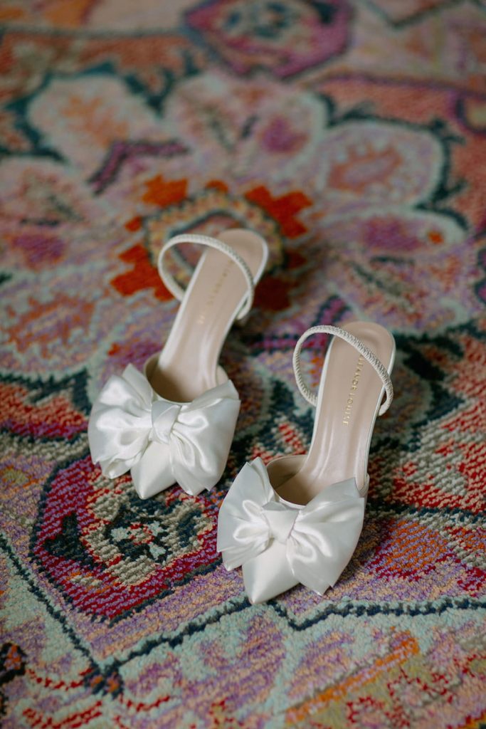 White bridal bow shoes on patterned rug during wedding morning preparations