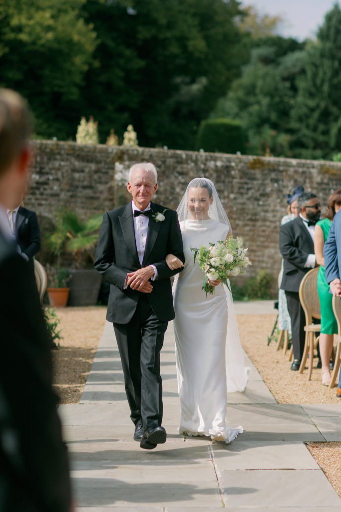 Bride walking down the aisle with a family member during outdoor wedding ceremony at Ripple Court Estate in Kent