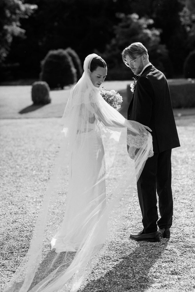 Bride and groom adjusting veil during outdoor wedding portraits