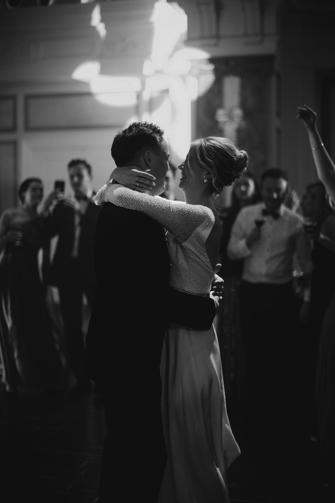 Bride and groom sharing first dance surrounded by guests with bride wearing relaxed updo and natural glowing bridal makeup