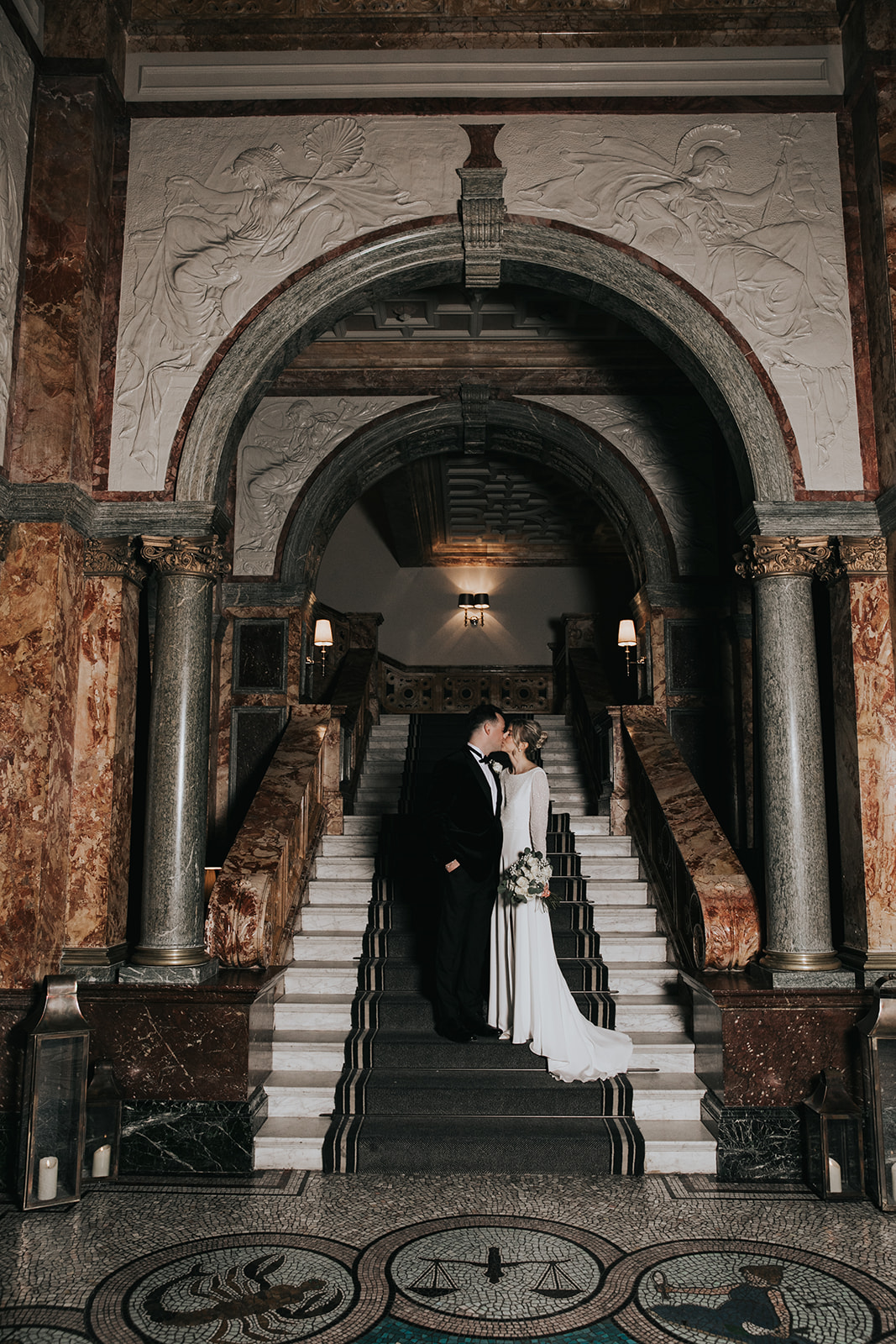 Bride and groom portrait on grand marble staircase at Kimpton Fitzroy London with bride wearing timeless updo and soft luminous makeup