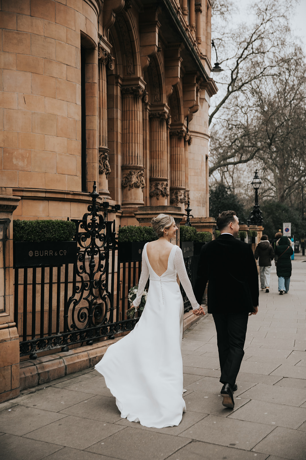 Bride and groom walking hand in hand outside Kimpton Fitzroy London on wedding day with bride wearing soft updo and fresh natural makeup