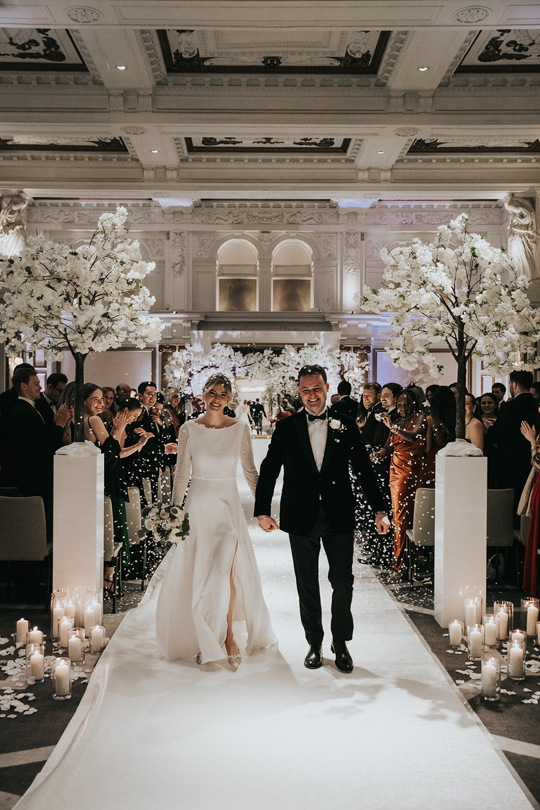 Bride and groom confetti walk down ceremony aisle at Kimpton Fitzroy London with bride wearing relaxed updo and glowing bridal makeup