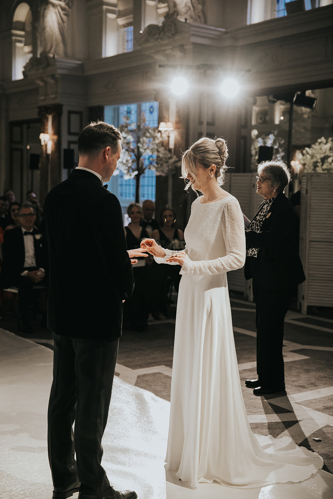 Bride placing ring on groom during ceremony at Kimpton Fitzroy London with soft natural makeup and classic bridal updo