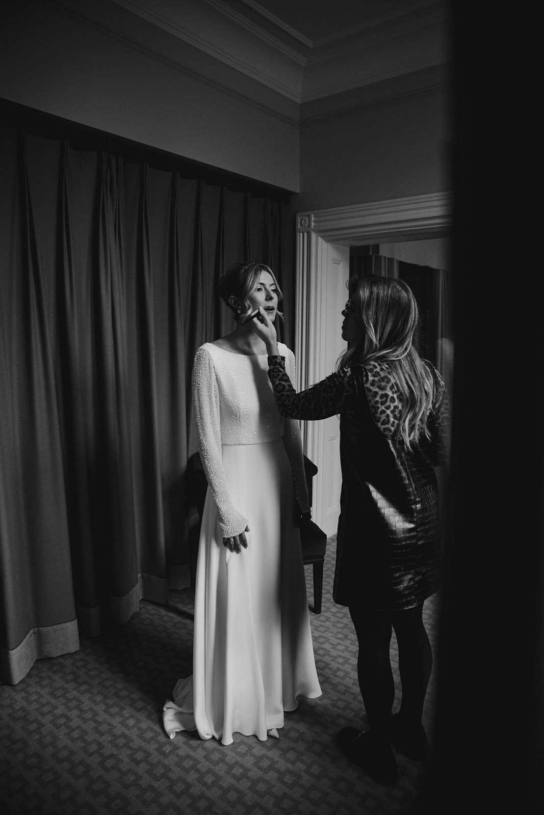 Makeup artist applying finishing touches to bride with soft natural makeup and elegant updo during bridal prep