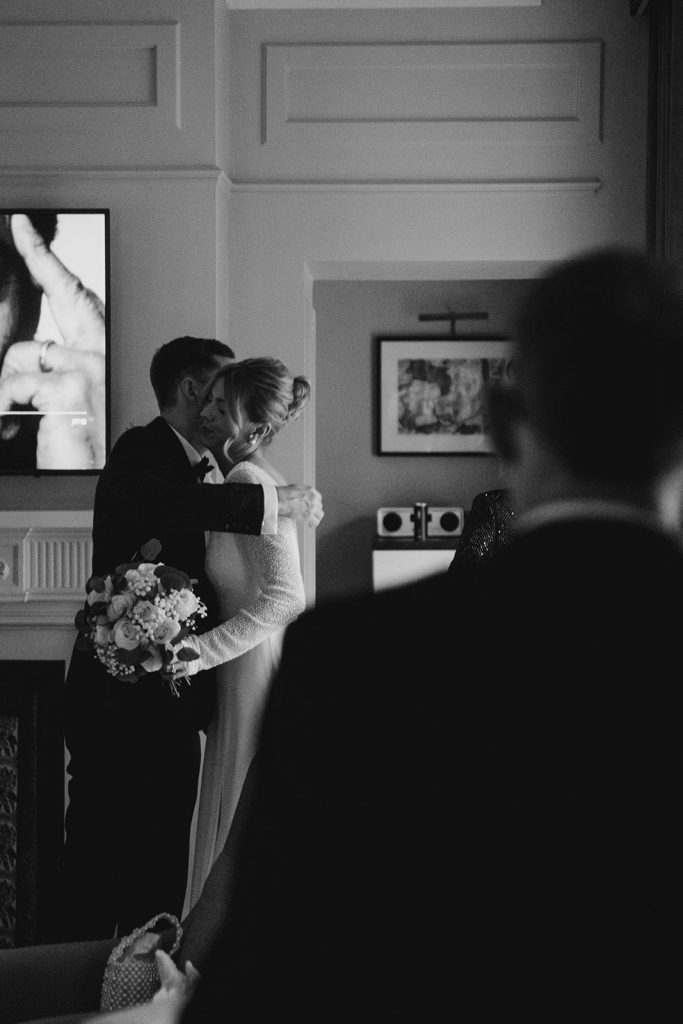 Bride embracing a guest at Kimpton Fitzroy London, showcasing a modern French twist hairstyle and soft glowing natural bridal makeup